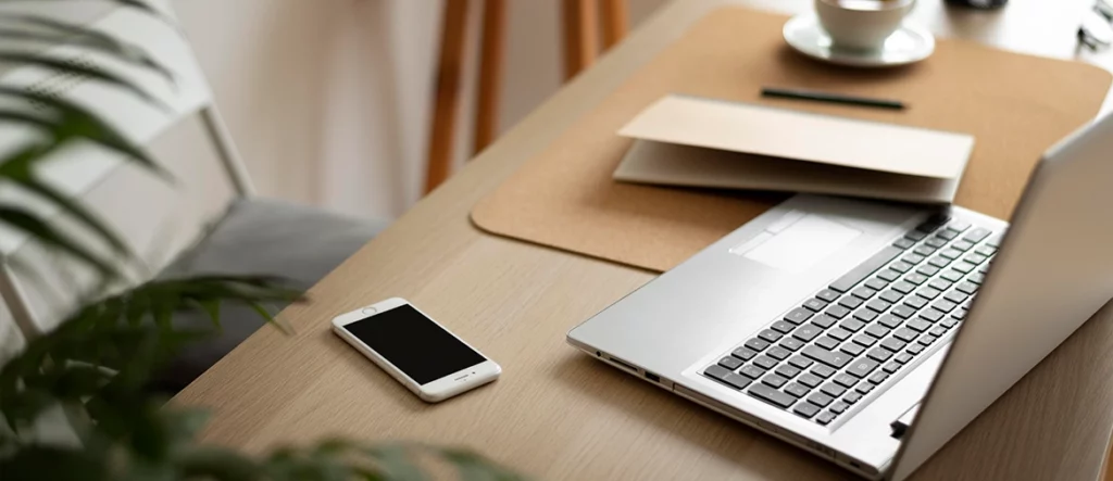 Bureau de télétravail minimaliste avec ordinateur portable, téléphone, et plante verte, favorisant le bien-être au travail.